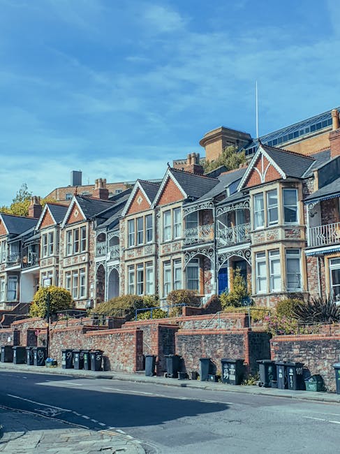 Exterior view of a row of colorful Victorian residential buildings on Chiswick High Road, featuring large bay windows with white trims, brick facades, and decorative cornices. The buildings are painte